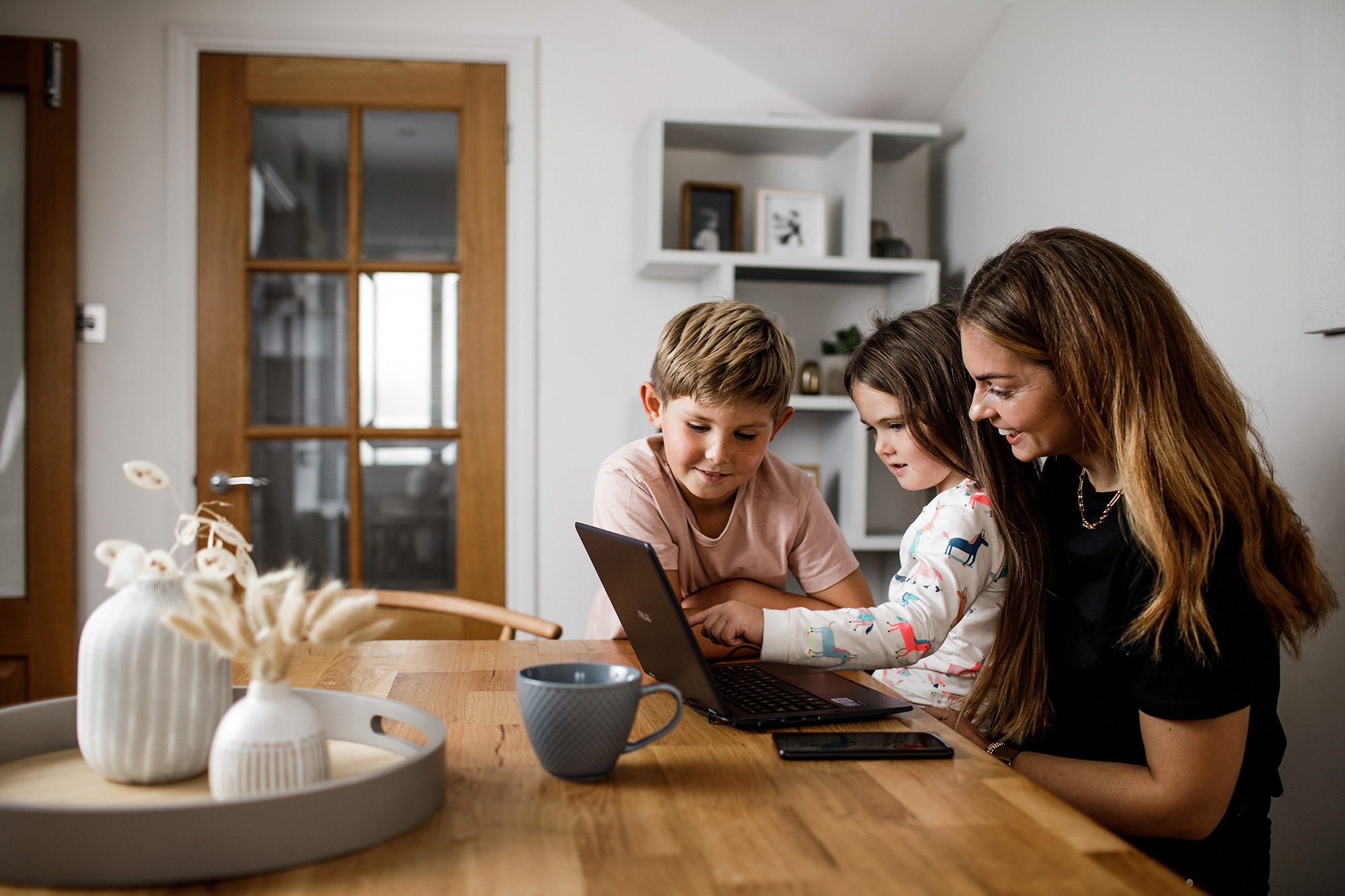 A mother and her children sat at the kitchen table enjoying something on a laptop computer.