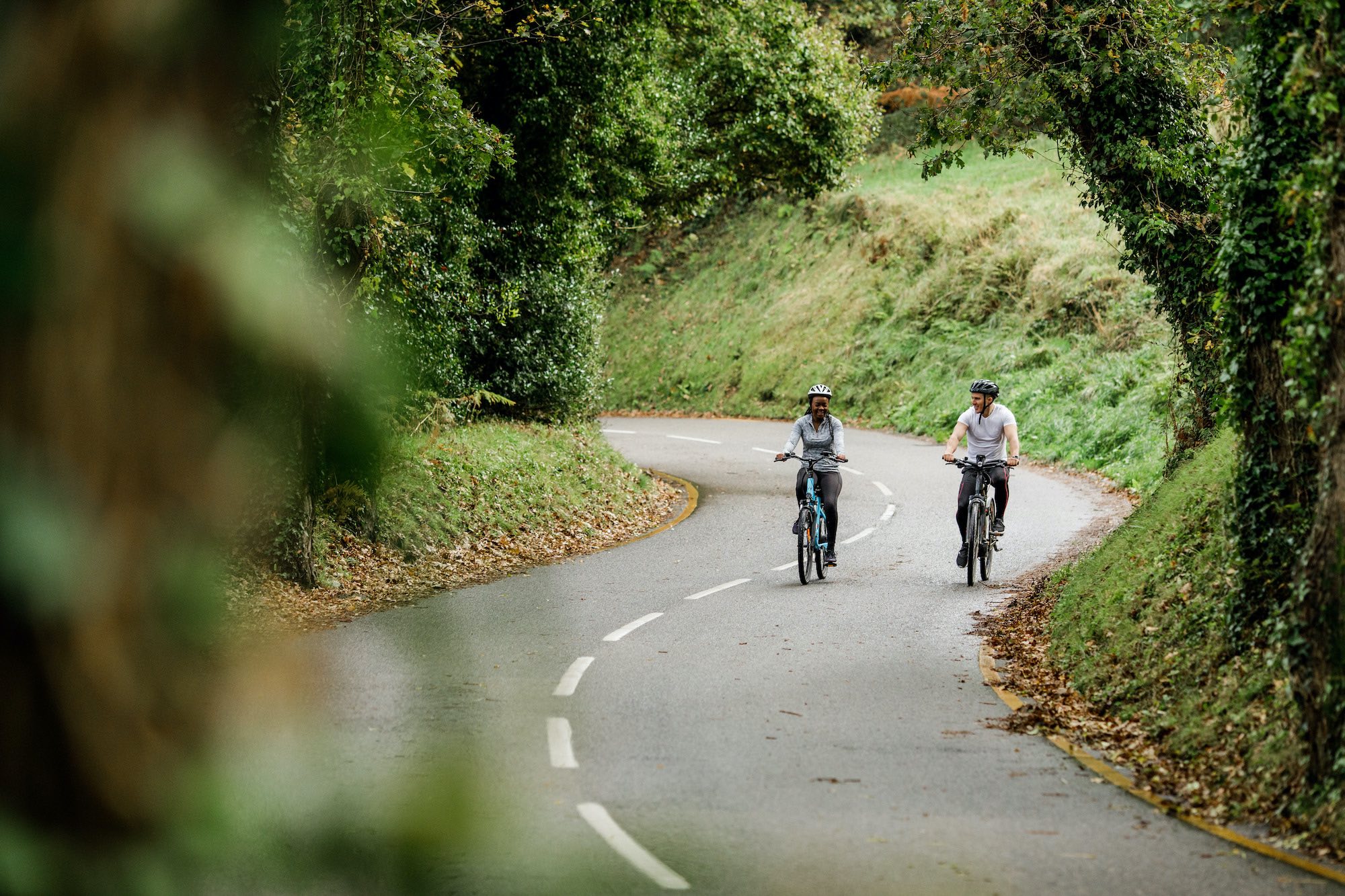 Two people ride electric bikes on quiet country road