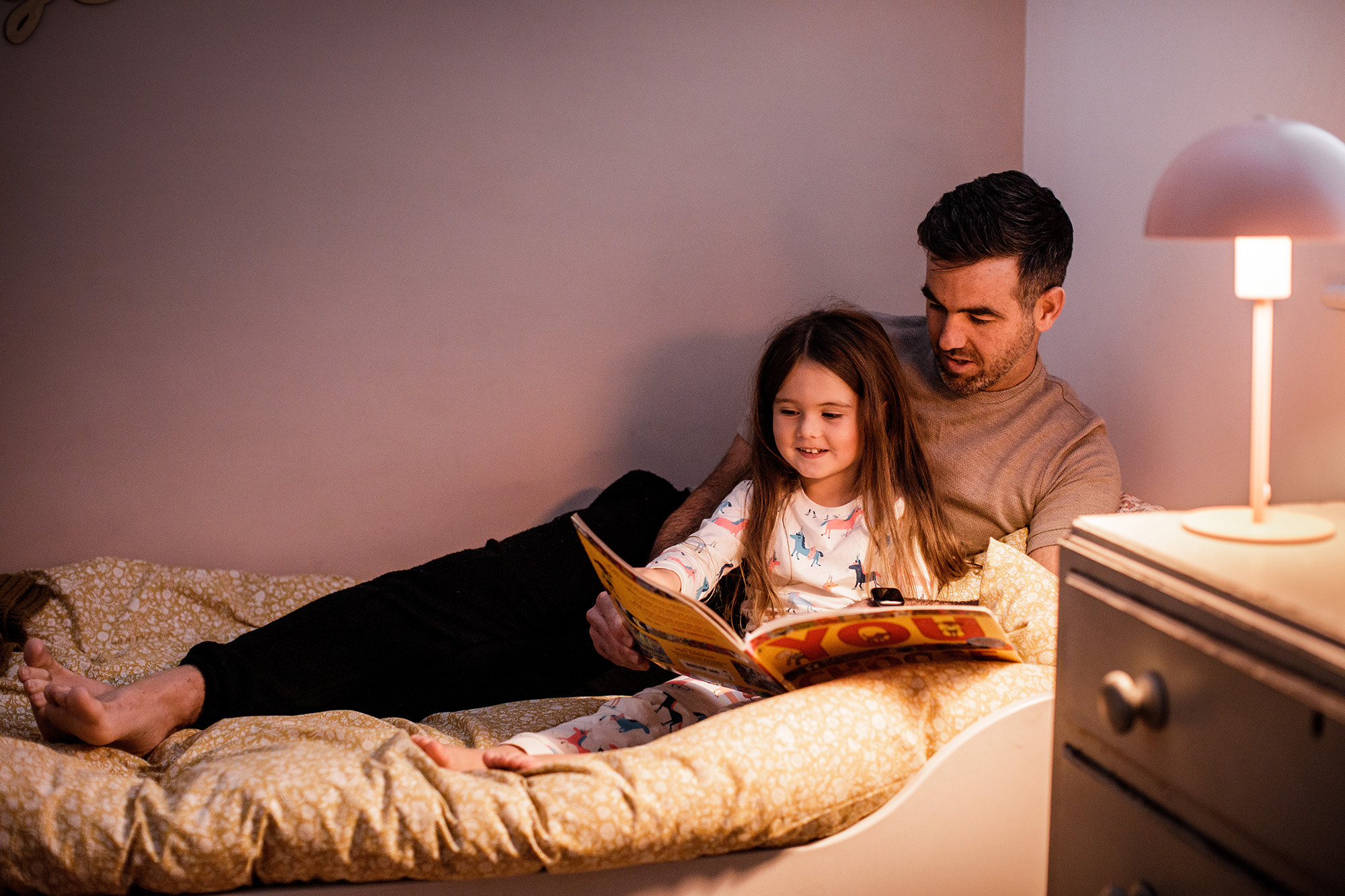 A father reads a story to his daughter in bed.