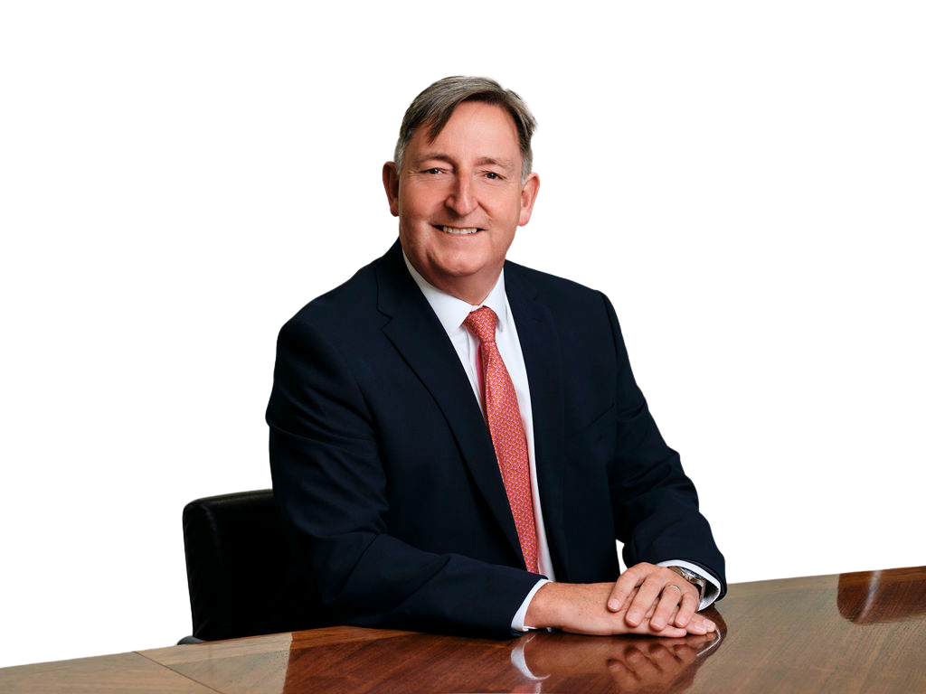 Paul Savery wearing a dark suit and red tie seated at a table. The background is white