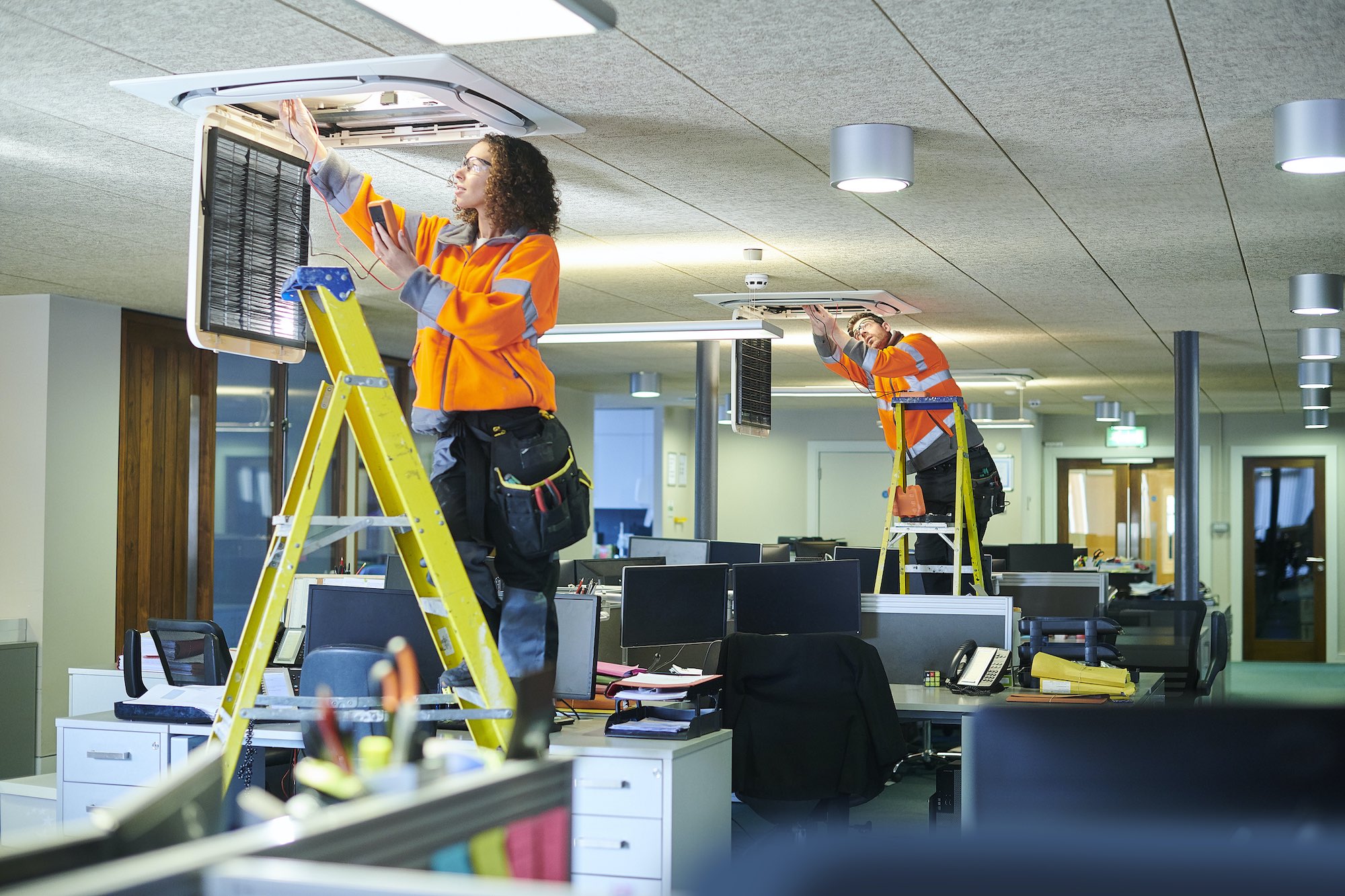 Two trades people install commercial air conditioning units in an office