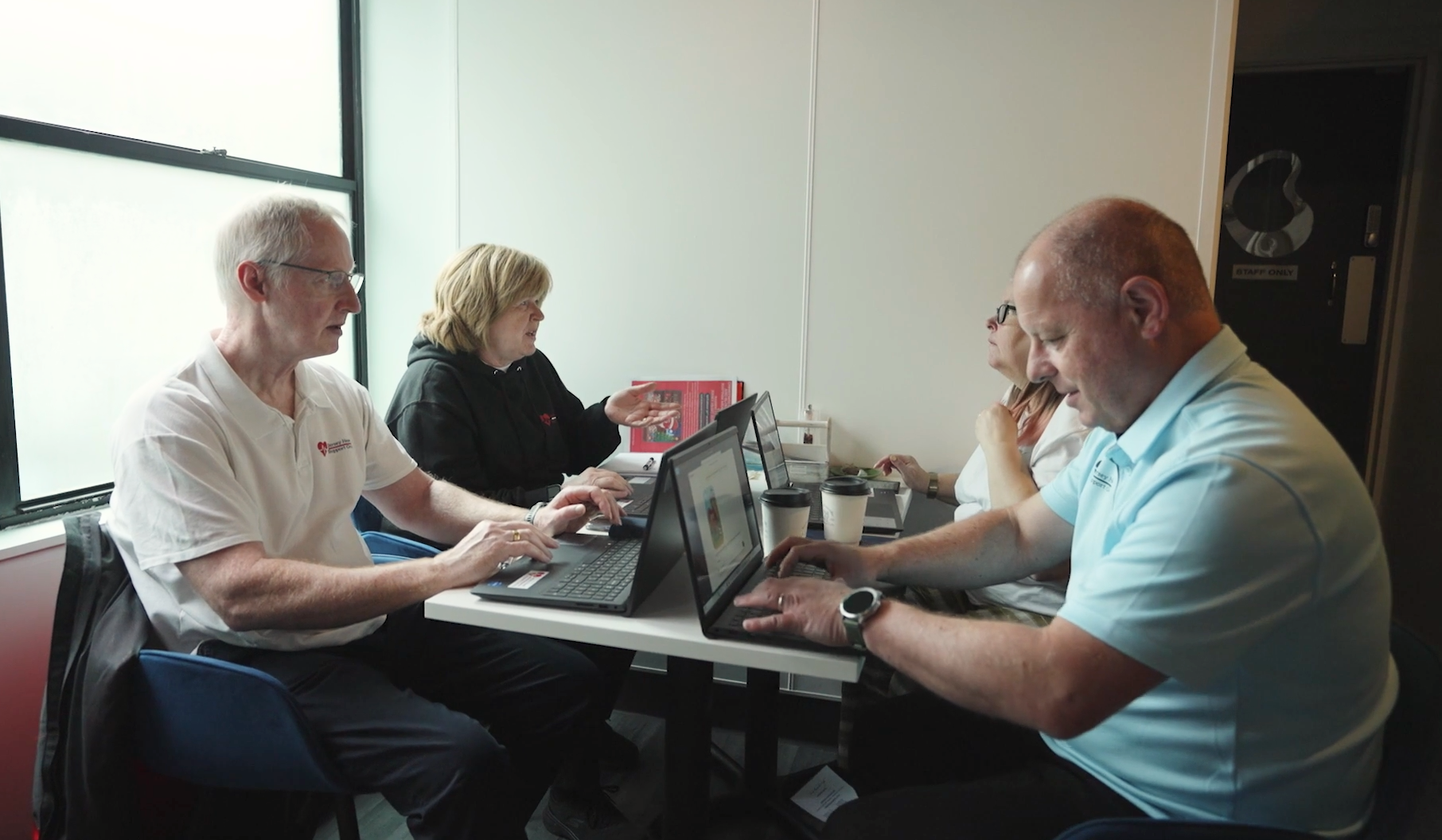 Four people gather around a table with their new laptops, they are talking amongst themselves and are happy to be doing work.