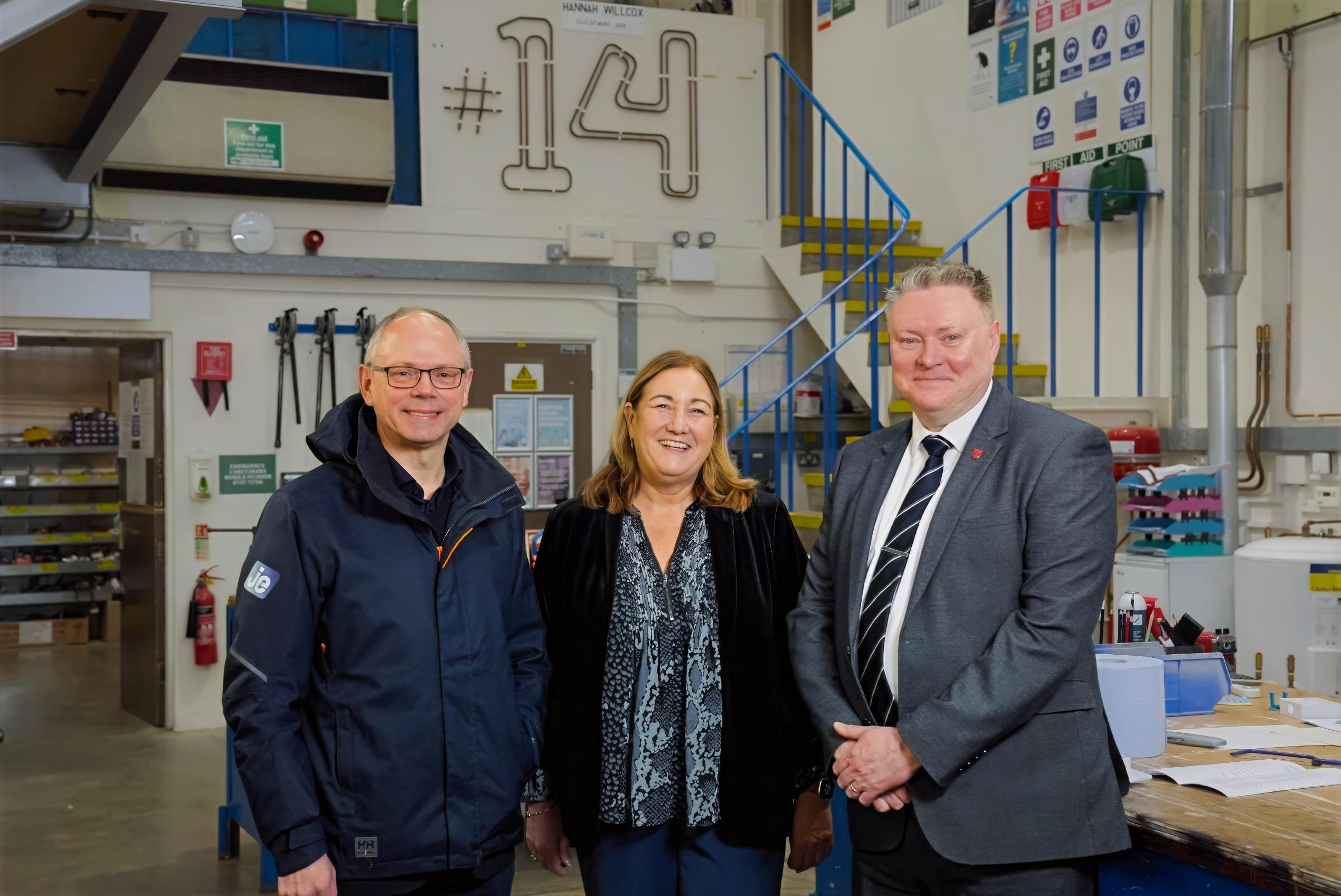 Three people looking at the camera, smiling and standing in a workshop