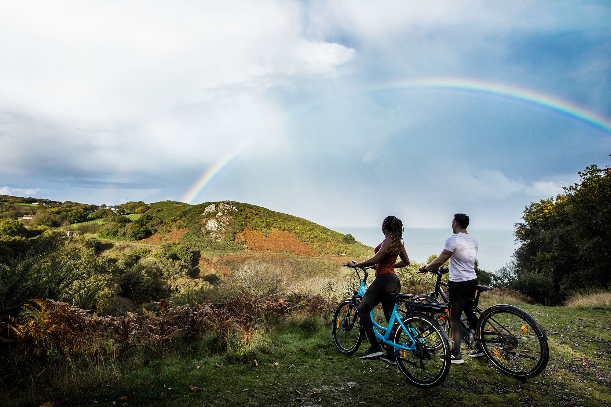 Couple on electric bikes look at rainbow in the countryside