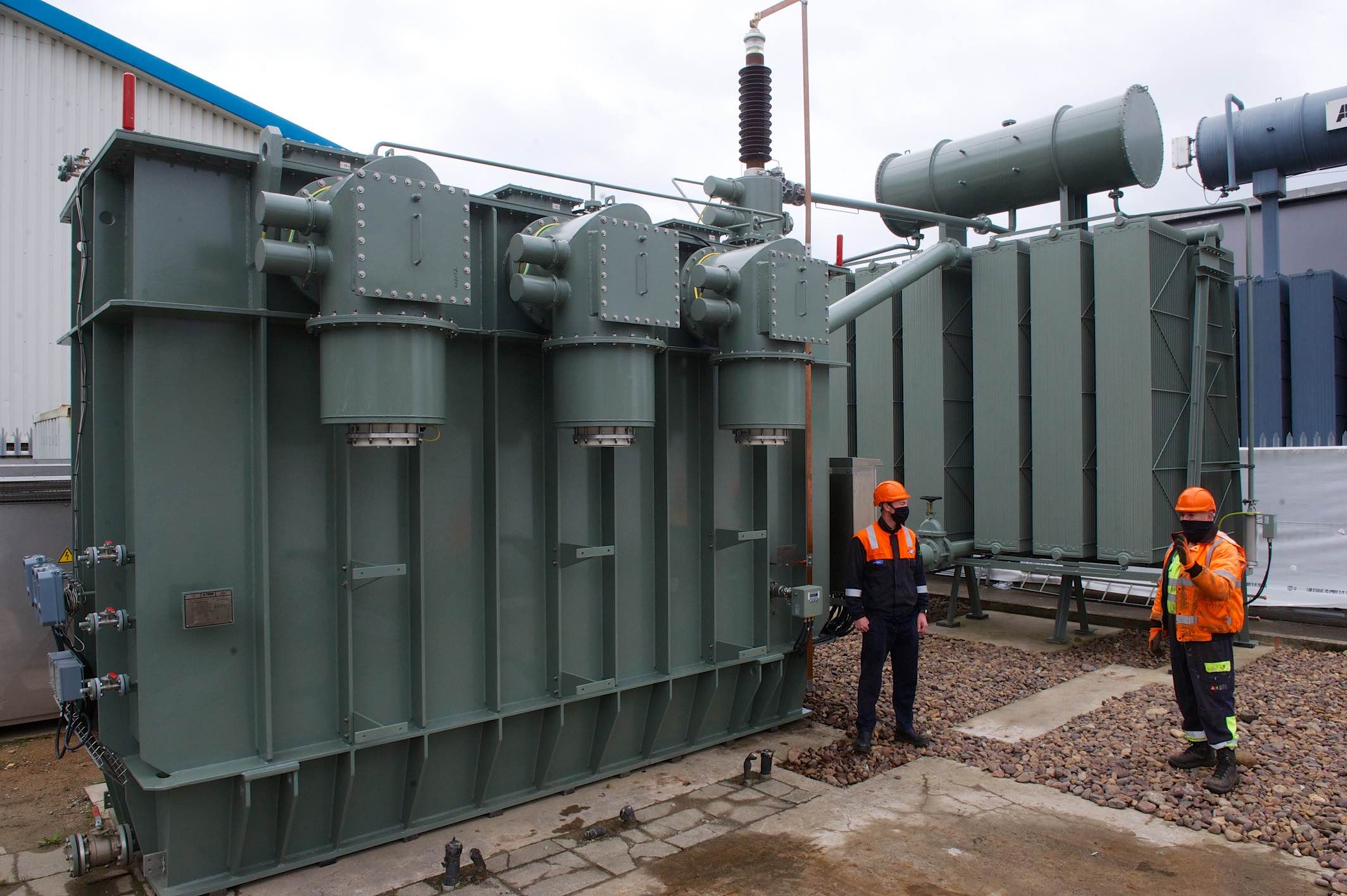 Two workers examine a large electricity transformer