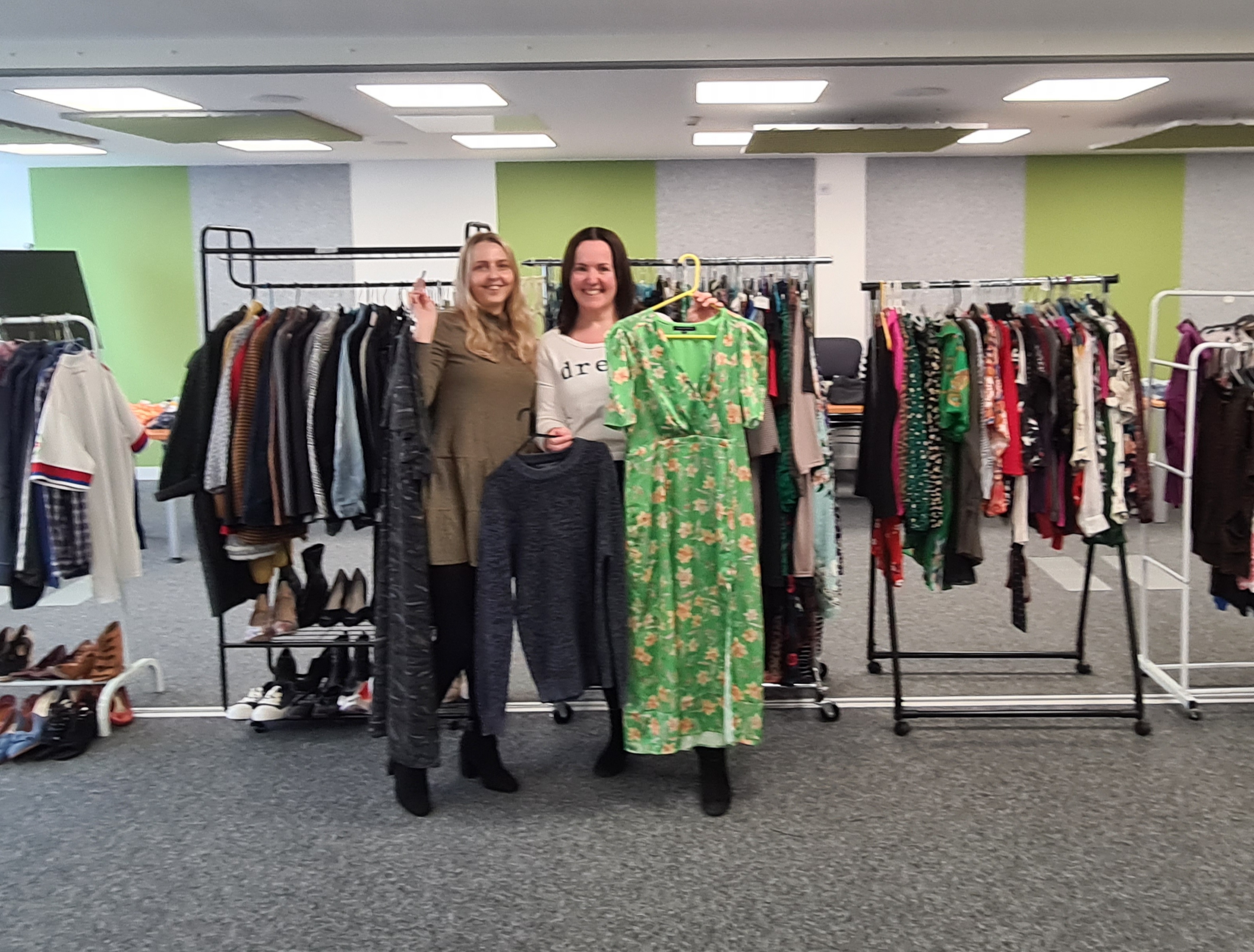 Image of Chloe Dunderdale and Sarah Le Gresley at the JE clothes swap. Behind them are rails packed full of donated clothes