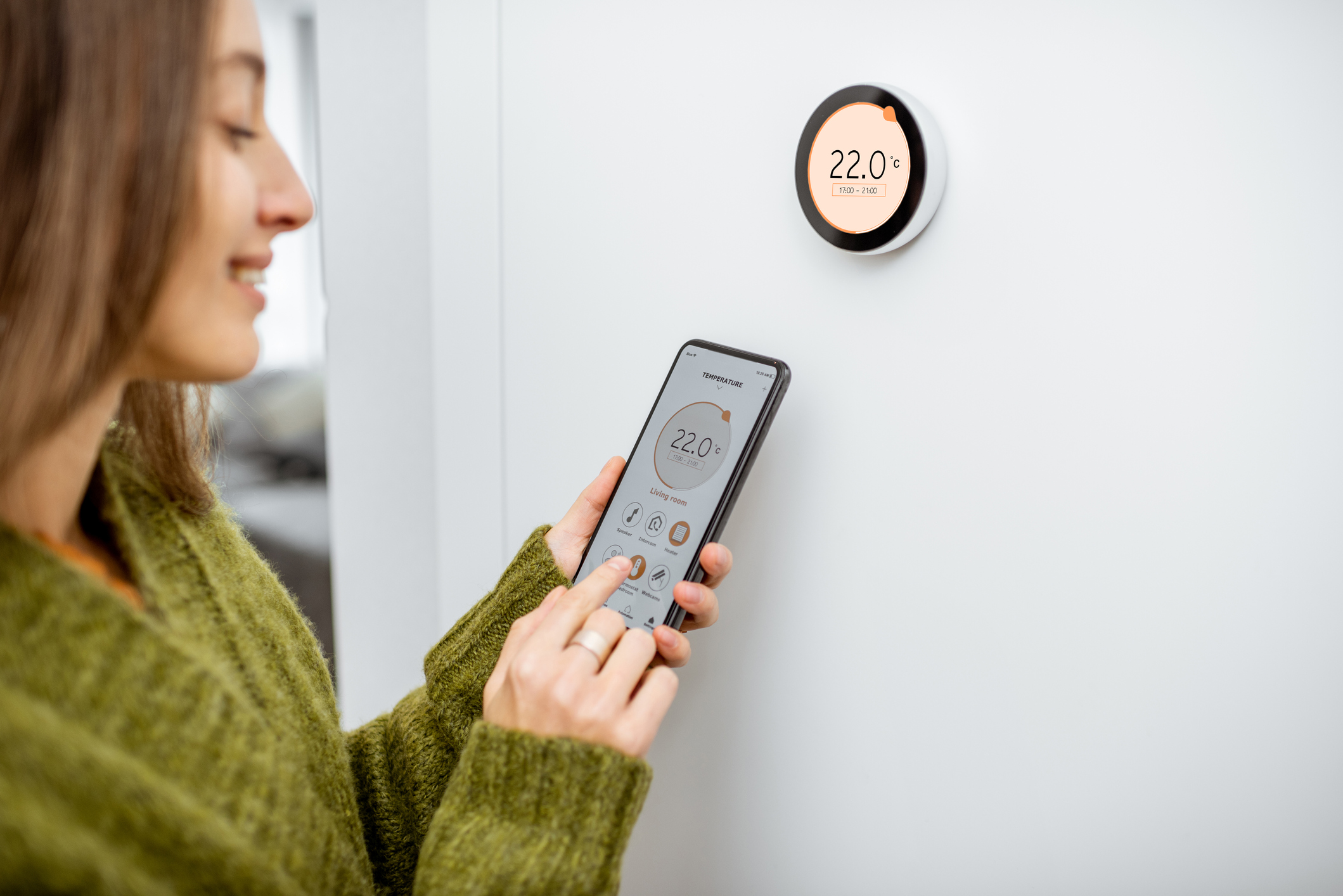 A young woman uses her phone to control her smart heating system.