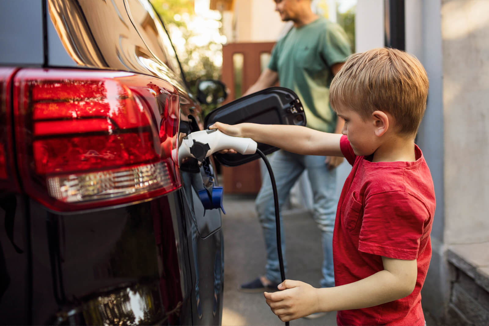 Child in red shirt plugs an electric vehicle charger into a car