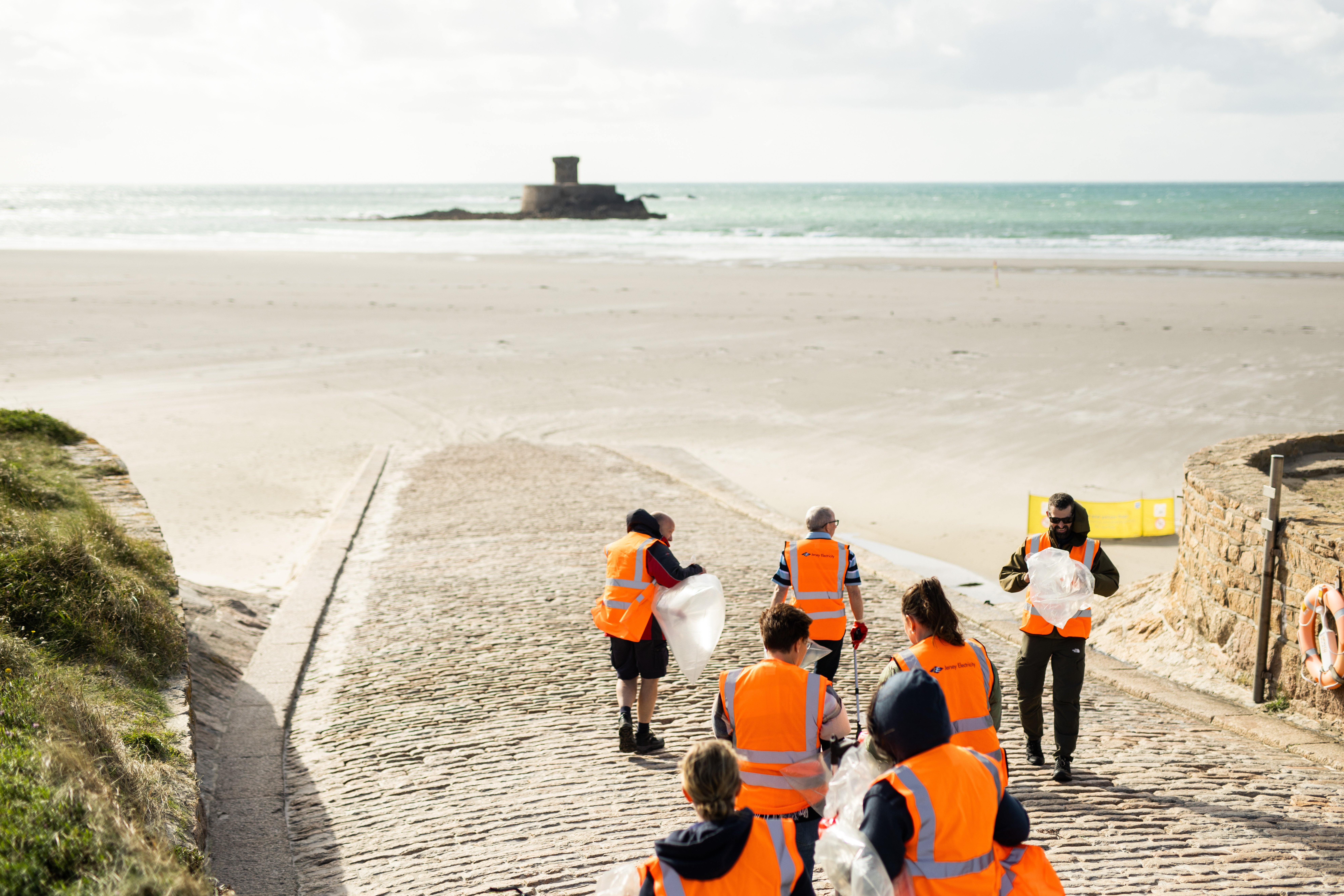 A group of people wearing high vis jackets, standing on a beach slip way with the sea behind them