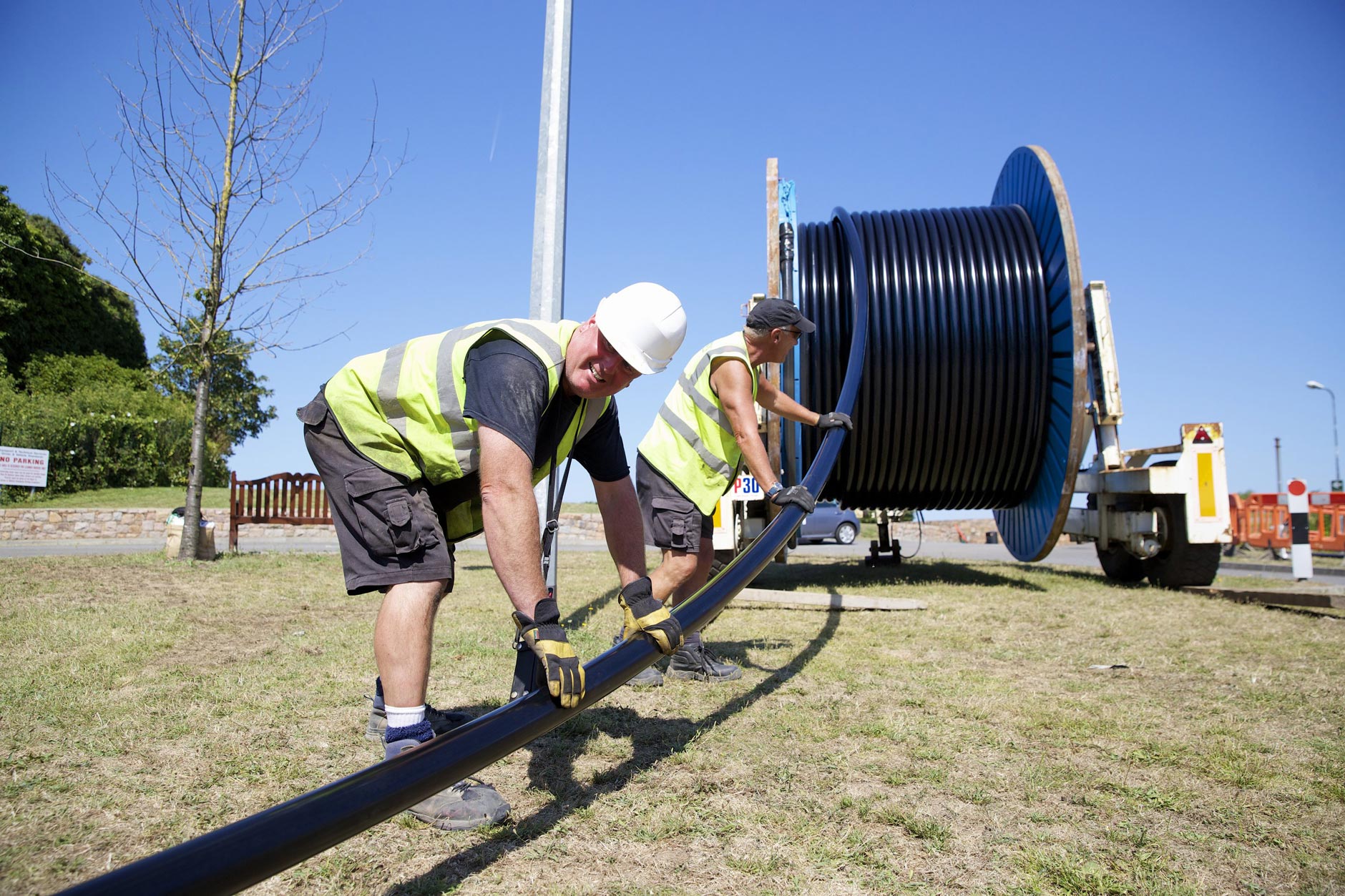 Two men guide power cable off a reel