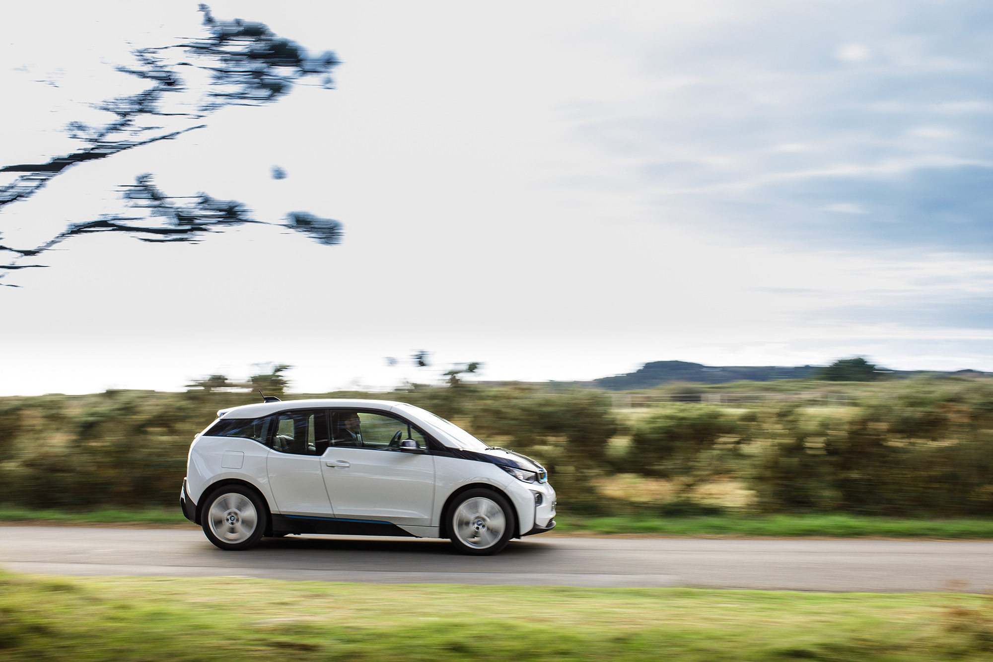 A white electric car drives along a road in Jersey.