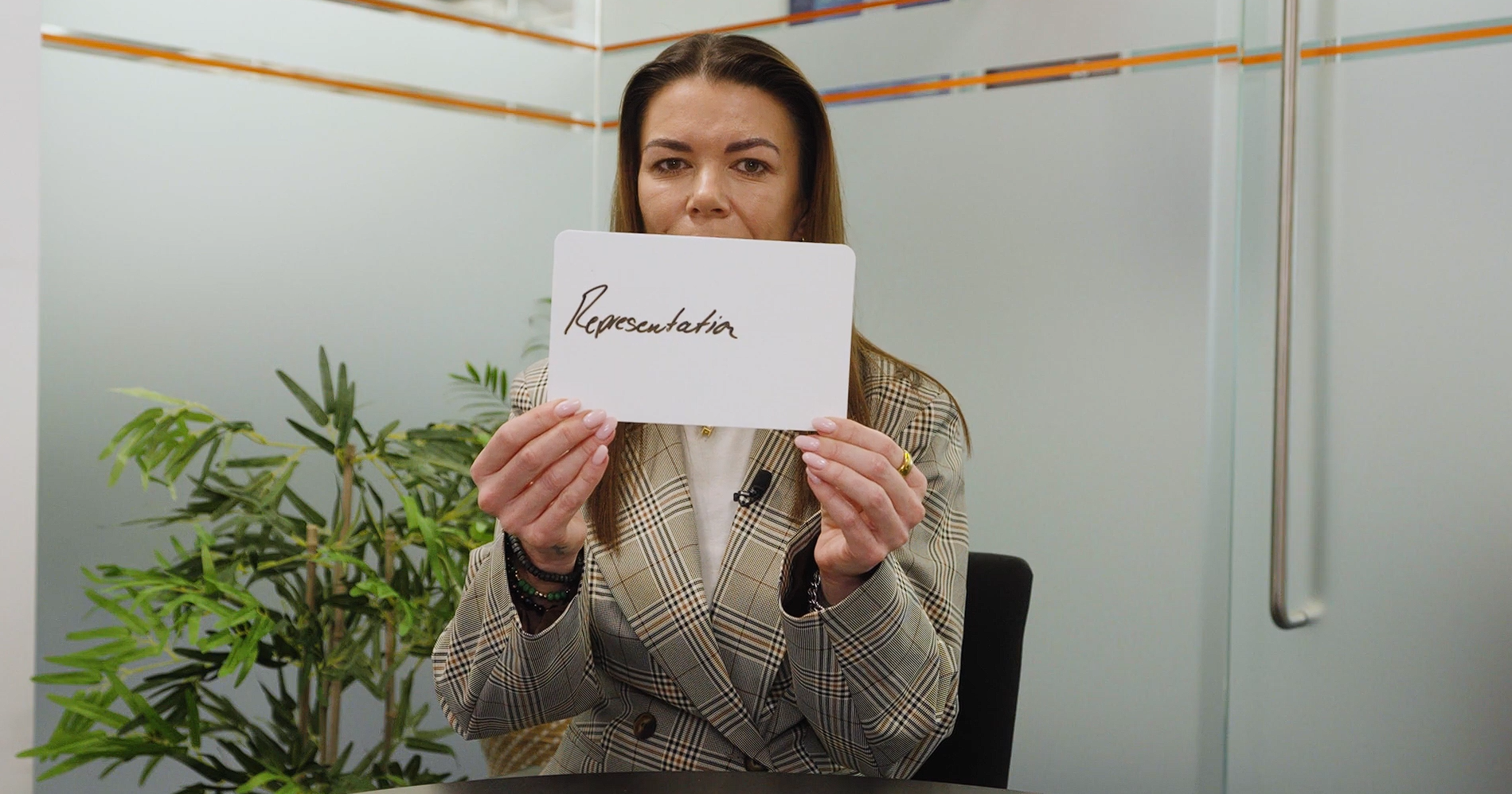 A person in an office setting holding a handwritten sign with the word 'representation'.