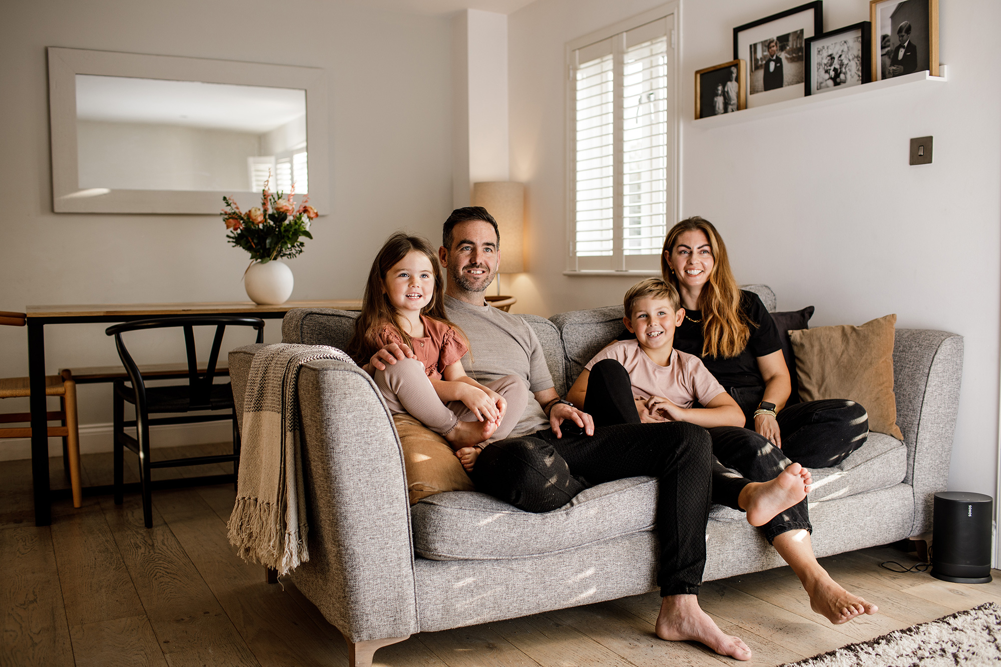 A family of four sit on the couch in their warm and cosy living room.